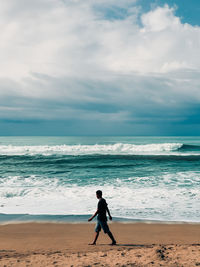 Rear view of woman walking at beach against sky