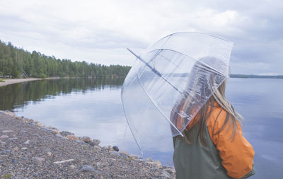 Rear view of woman standing by lake against sky