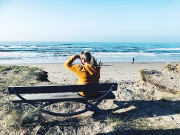 Man sitting on shore at beach against sky