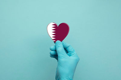 Close-up of hand holding heart shape against blue background