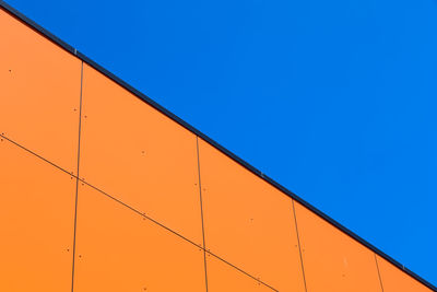 Low angle view of orange wall against clear blue sky