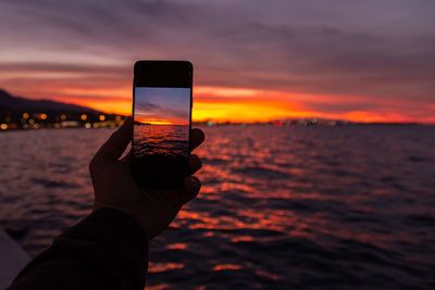 Midsection of person photographing sea against sky during sunset