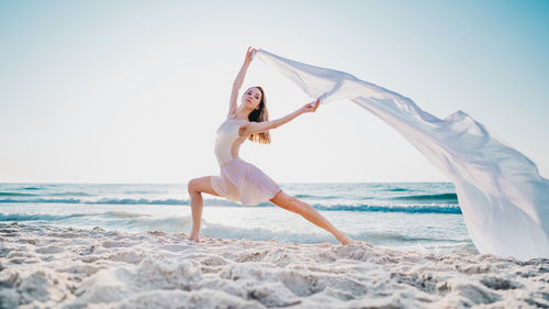 Woman dancing with textile on beach against sky