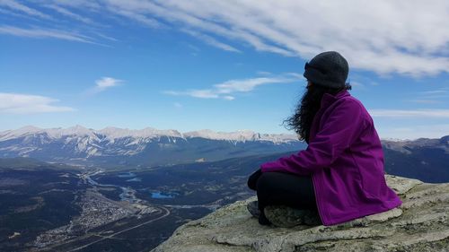 Woman sitting on top of mountain against sky