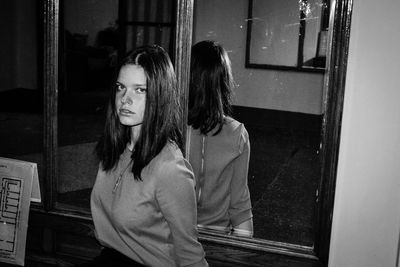 Portrait of young woman standing against mirror at home