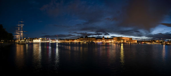 Illuminated buildings by river against sky at night