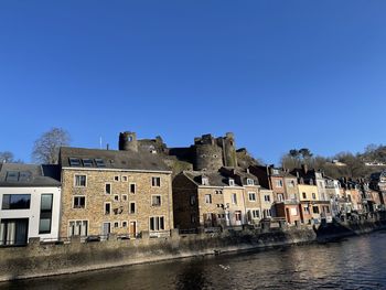 Buildings by river against clear blue sky