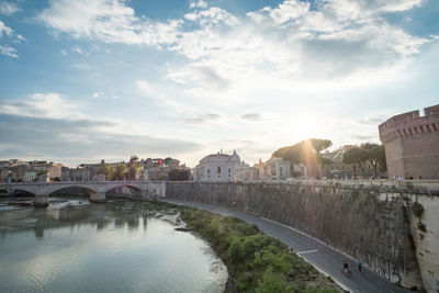 Bridge over river by buildings in city against sky