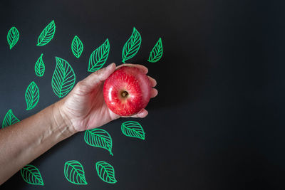 Close-up of hand holding strawberry over black background