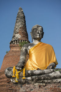 Low angle view of buddha statue and stupa against clear blue sky
