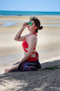 Woman sitting on beach in red bikini and blue sarong