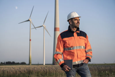 Male engineer holding digital tablet while standing in front of wind turbines