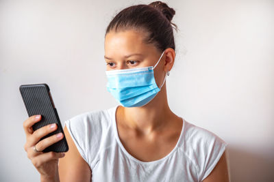 Young woman wearing mask using smart phone against wall
