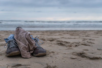Shoes on sand at beach against sky
