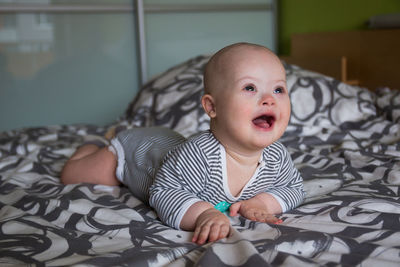 Cute baby boy looking away lying on bed at home