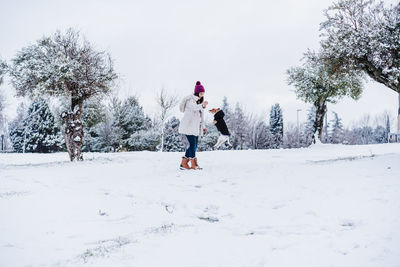 Woman in snowy mountain wearing modern coat. playing with cute jack russell dog. winter season.