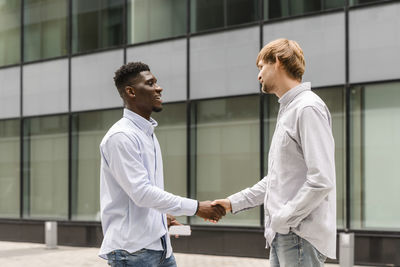 Young man doing handshake with friend on footpath