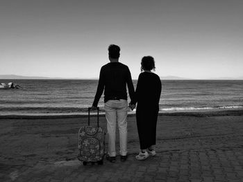 Rear view of friends standing on beach against clear sky