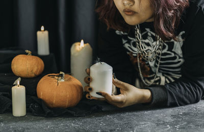 Young asian woman in costume witch blows out the candles on black cloth background of halloween