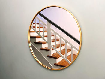 Close-up of a round mirror on a wall reflecting a wooden staircase 