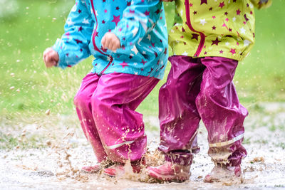 Low section of children playing in puddle on field