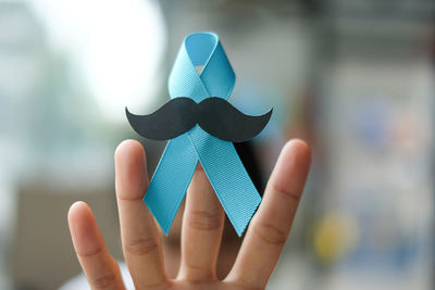 Cropped image of hand holding blue ribbon with mustache