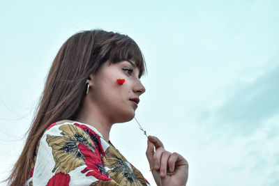 Portrait of young woman looking at camera against sky