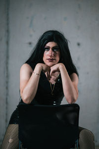 Portrait of young woman sitting against wall