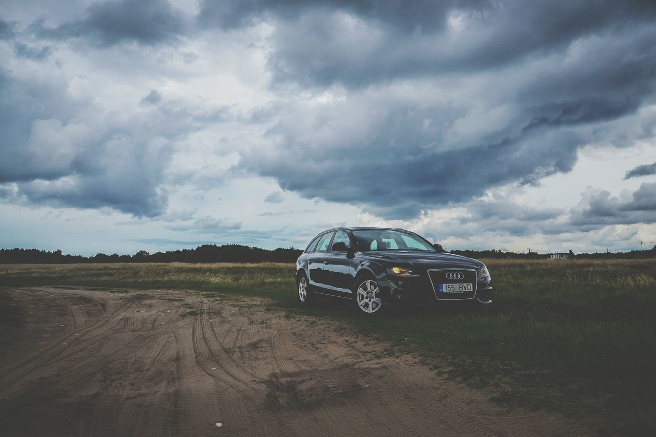 CAR ON FIELD AGAINST STORM CLOUDS OVER LANDSCAPE