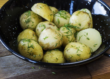 High angle close-up of boiled potatoes with dill served in bowl on wooden table