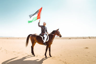 Man riding horse on beach against clear sky