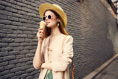 Young woman wearing sunglasses standing against brick wall