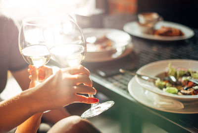 Cropped hands toasting wineglass by table