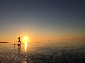 Silhouette person on sea against sky during sunset