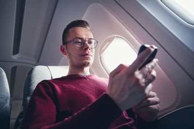 Low angle view of man using phone in airplane