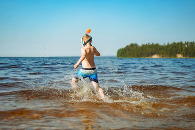 Cute caucasian boy wearing snorkel mask running into water with splashes. vacation on sea side.