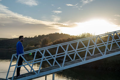 Man standing on bridge against sky during sunset