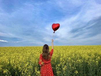 Woman in red dress standing in a field of canola flowers and holding a red heart balloon