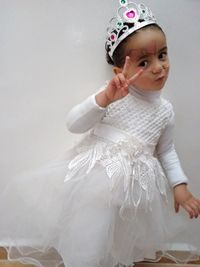 Portrait of cute girl wearing white dress while standing against wall