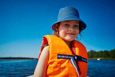 Portrait of cute girl wearing life jacket against cleat blue sky