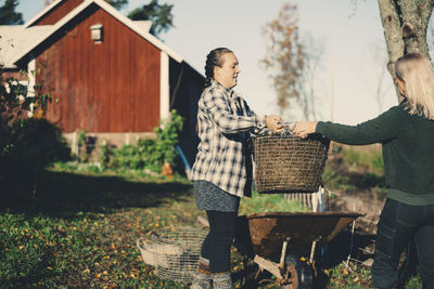 Mid adult female farmer handing basket full of straw to friend at organic farm