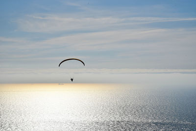 Distant view of silhouette person paragliding over sea against sky