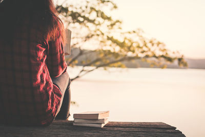 Midsection of woman with book sitting at lake