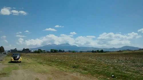 Cars on road by field against sky