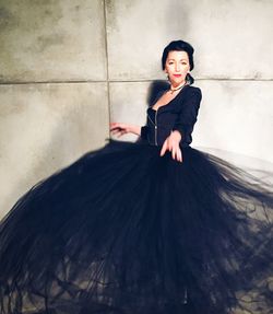 Portrait of young woman wearing black gown against wall