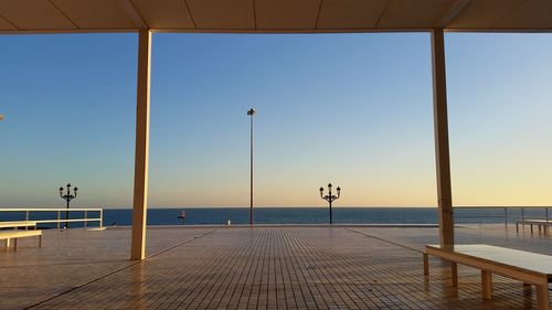 Empty benches on promenade by sea against clear sky during sunset