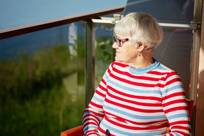 Elderly woman in glasses sitting on balcony near the sea