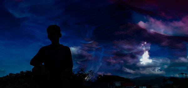 Rear view of silhouette man standing against sky at night