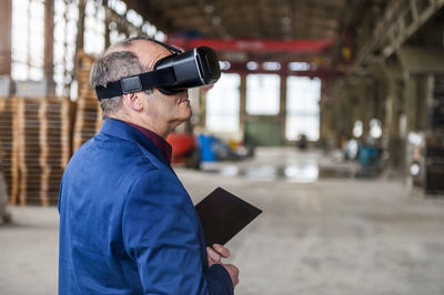 Manager standing in factory hall looking through vr glasses