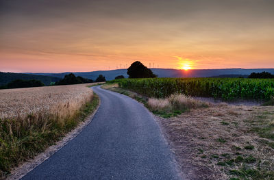 Empty road amidst field against sky during sunset